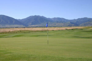 Well-manicured green with flag pin, featuring mountains in the background.