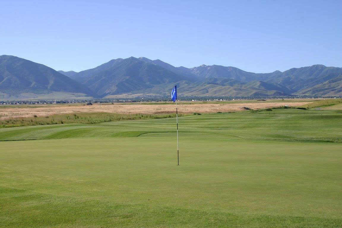 Well-manicured green with flag pin, featuring mountains in the background.