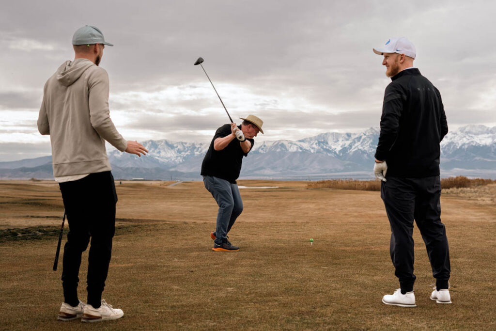Golfer, mid-swing, teeing off while 2 other golfers watch.